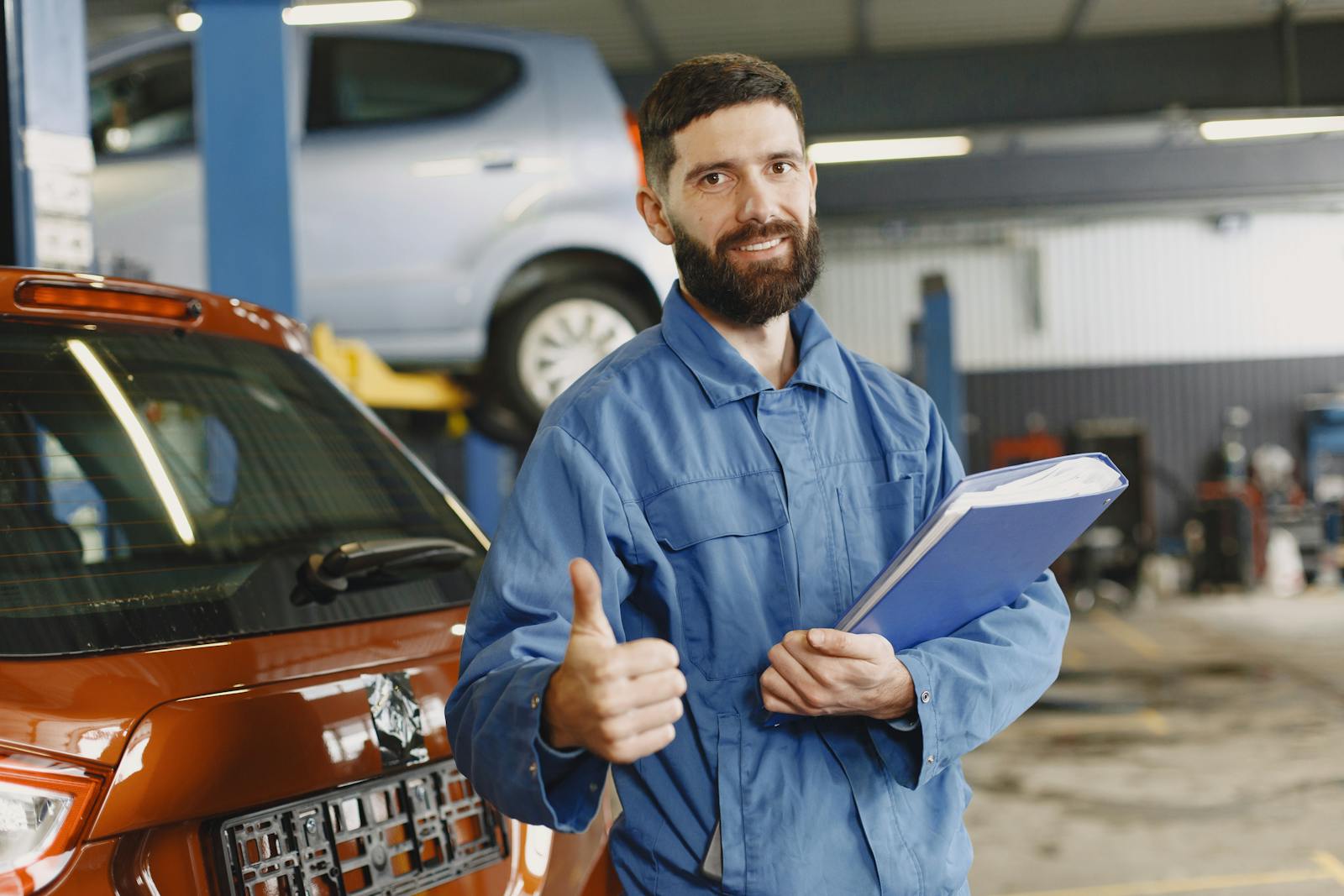 Man in Blue Coveralls Standing in an Auto Repair Shop Doing an Ok Hand Gesture